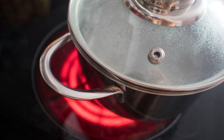 Saucepan On Top Of An Electric Resistance Stove. Glowing Hot Coils Can Be Seen Through The Surface Of The Cooktop.