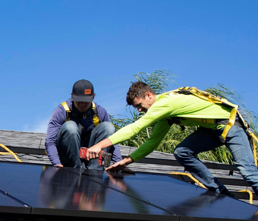 Two workers installing solar panels on a roof