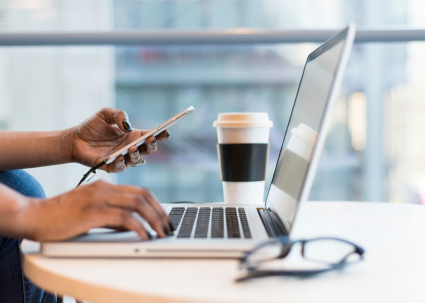 Person Looking At Laptop With Phone In Hand