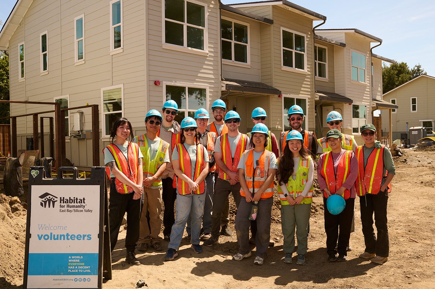 Ava staff wearing hard hats and orange safety vests smiling in front of Sequoia Grove town homes and a Habitat for Humanity Volunteers sign