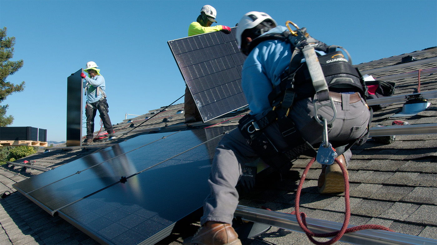Three Men Installing Solar Panels On The Rooftop Of A Townhome.