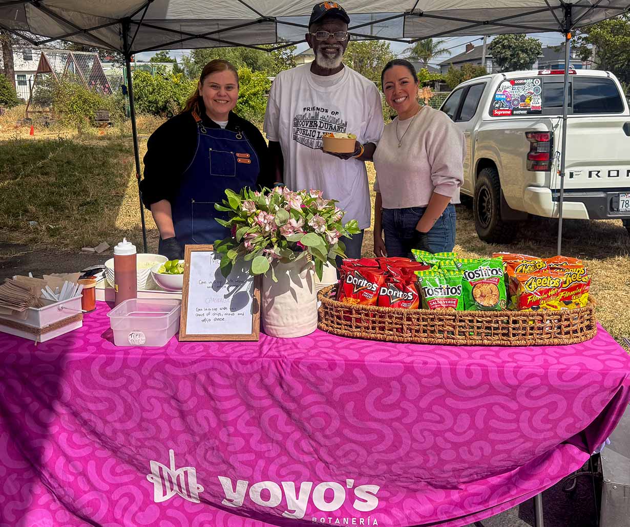 Yoyo's Botaneria Staff Stand Behind Their Booth, Smiling, With A Member Of The Community Holding A Chaska Corn Bowl